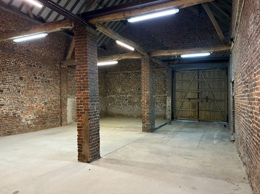 Beschikbaar: een droge en veilige schuur/atelier van 150 m², uitgerust met een grote toegangspoort en een vrije hoogte van 7 meter. De ruimte beschikt