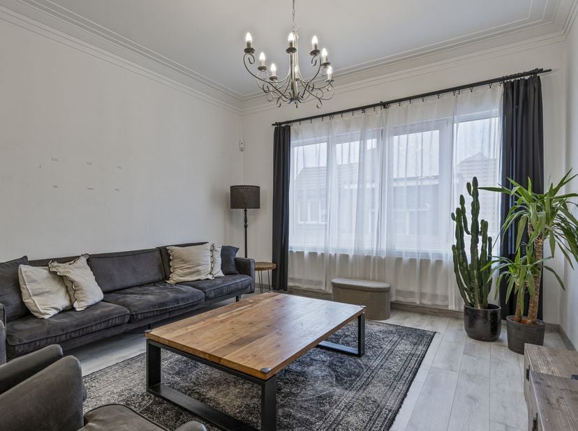 Via de trap bereikt u de eerste verdieping waar de inkomdeur van het appartement zich bevindt. De hal leidt u naar de lichtrijke leefruimte, waar hoge