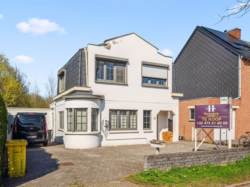 Wie de oprit van dit mooie, wit geschilderde huis met overdekte inkom en kleinhouten in de ramen oprijdt, ziet meteen dat er hier vier auto&#039;s geparkee