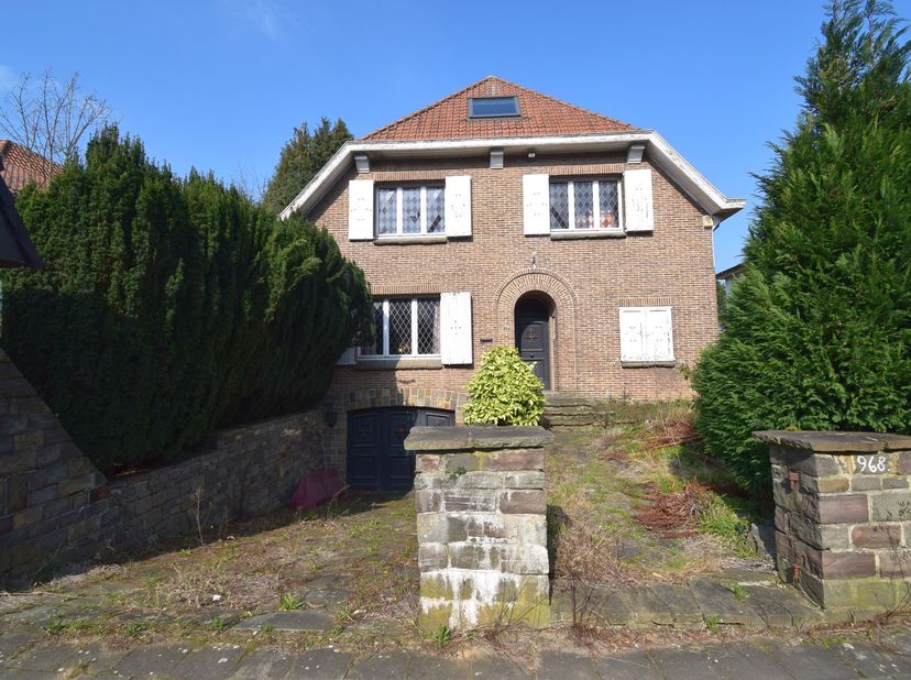 Chaussée romaine 968 : Villa 4-façades à rénover offrant 170m² habitables + grenier, cave intégrale (dont un garage de 50m²) et jardin. Au rez-de-chau
