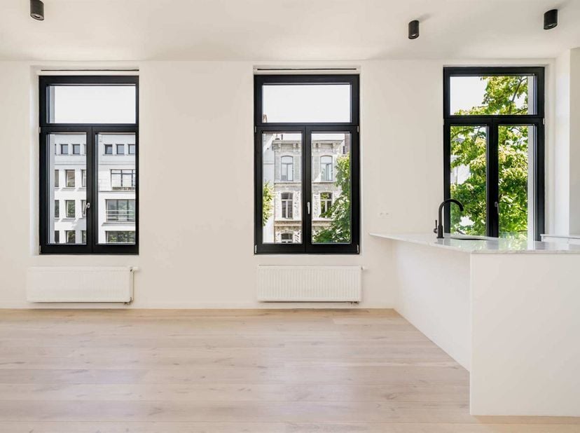 Het appartement baadt in licht dankzij hoge plafonds en grote raampartijen. Het is gelegen op de 2de verdieping en kijkt uit over de rustige Emiel Ban