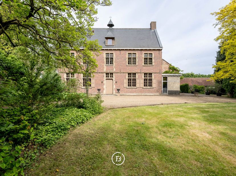 In het hart van Sint-Kornelis-Horebeke, verscholen achter het dorpsplein, ligt dit uitzonderlijk herendomein met bijgebouw op een volledig omwald terr