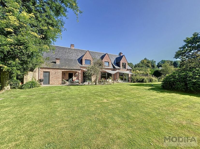 Gelijkvloers: 160m² – Natuursteen – HSP=2,70m<br />
Inkomhal<br />
Vestiaire / toiletten<br />
Woonkamer met open haard en toegang tot terras/tuin<br