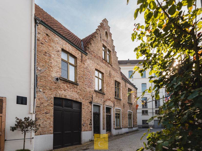 In een typische verkeersarme straat midden in het historische centrum van Brugge bevindt zich deze bijzonder sfeervolle stadswoning met authentieke tr
