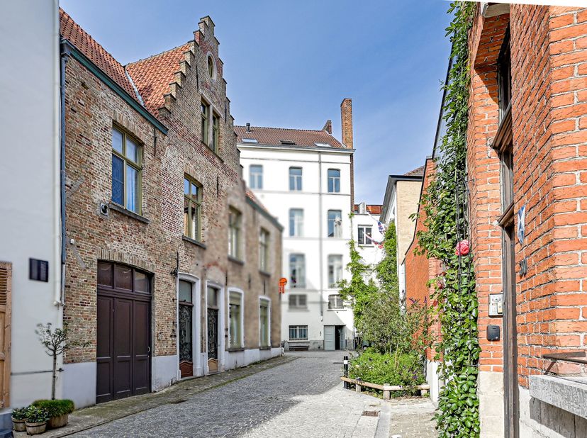 In een typische verkeersarme straat midden in het historische centrum van Brugge bevindt zich deze bijzonder sfeervolle stadswoning met authentieke tr