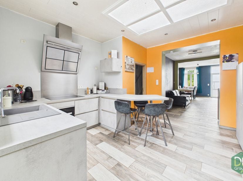 Op het gelijkvloers bevindt zich een eerste leefruimte van 27 m² die uitgeeft op een keuken, uitgerust met een oven, spoelbak, inductiekookplaat, damp