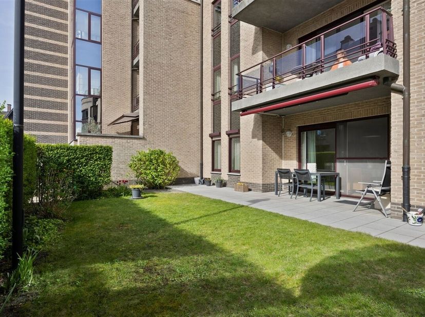 Uitzonderlijk ruim, gelijkvloers 2-slaapkamer appartement met terras en tuintje, zonnepanelen en inpandige garagebox gelegen vlakbij het centrum van M