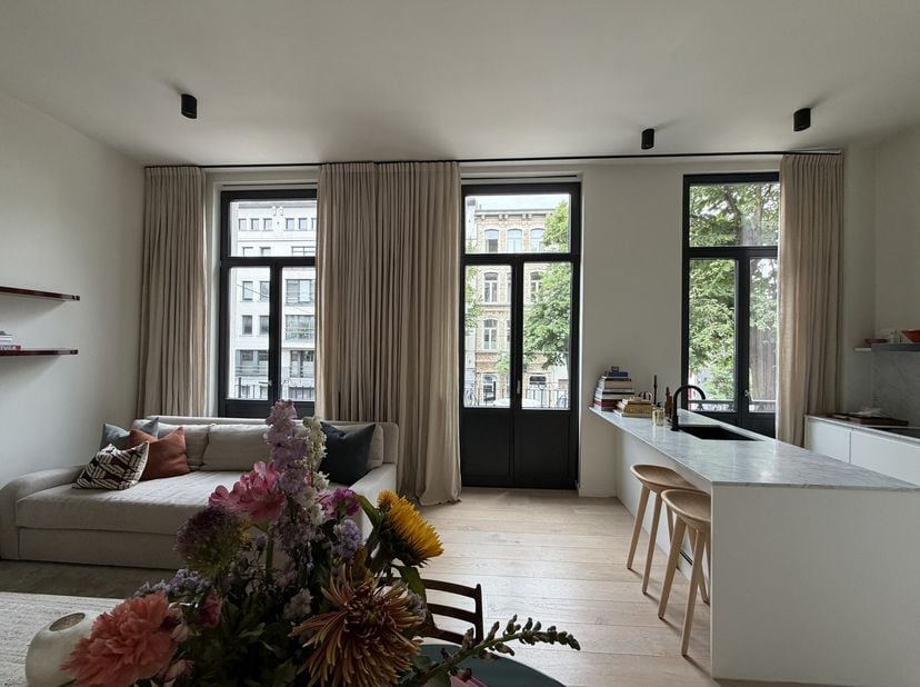 Het appartement baadt in licht dankzij hoge plafonds en grote raampartijen. Het is gelegen op de 1ste verdieping en kijkt uit over de rustige Emiel Ba