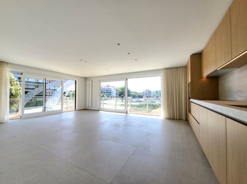 Magnifique appartement d'angle (104 m²) entièrement rénové, bénéficiant d'un emplacement central sur la place de l'Esplanade à La Panne. L'appartement