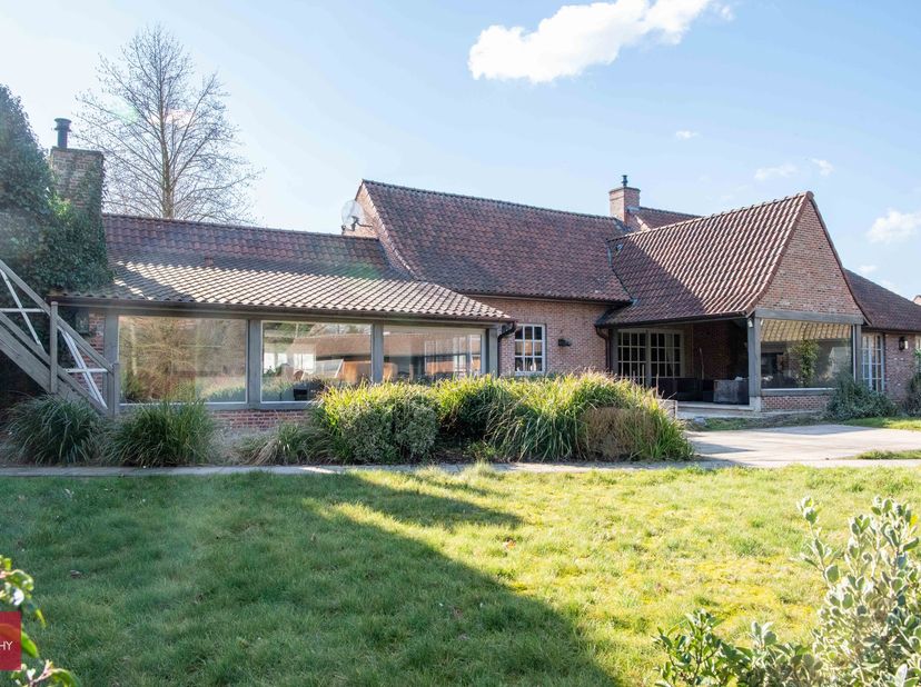 Bestaande uit inkomhal, living in Bourgondische dallen en cassette, eetplaats, bureelruimte met aquarel, ingerichte keuken met open haard, bijkeuken,